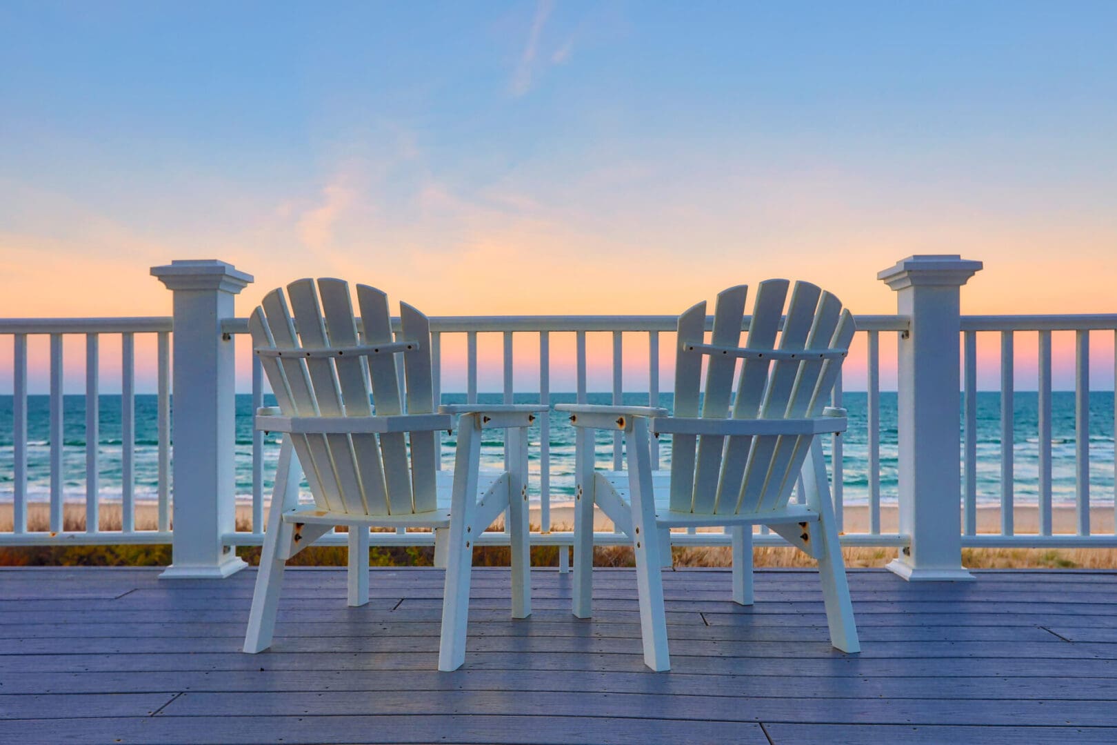 Two white lawn chairs on a porch overlooking the ocean.