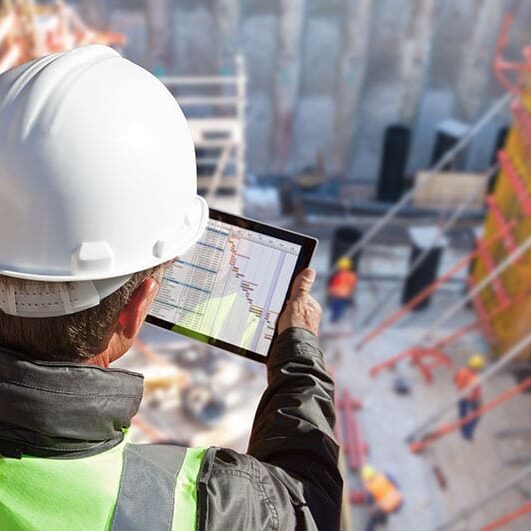 A man in hard hat looking at construction site on tablet.